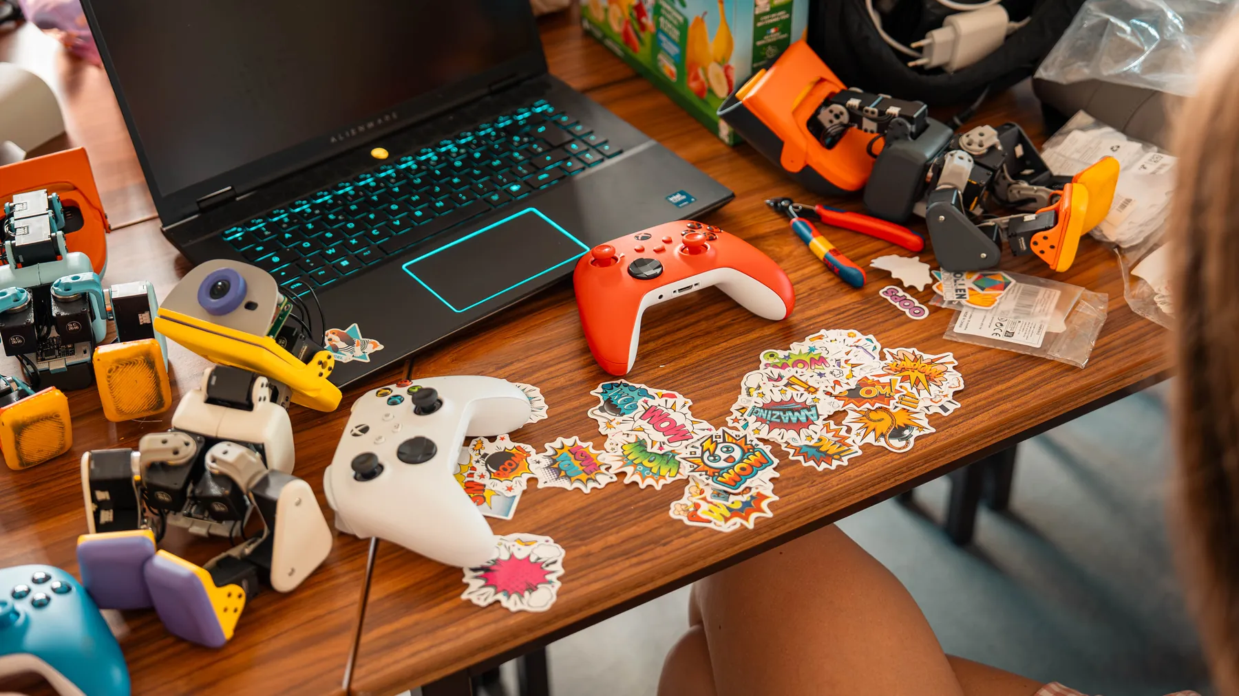 MicroDuck robots, game controllers, tools and a laptop on the official shoot’s workbench.