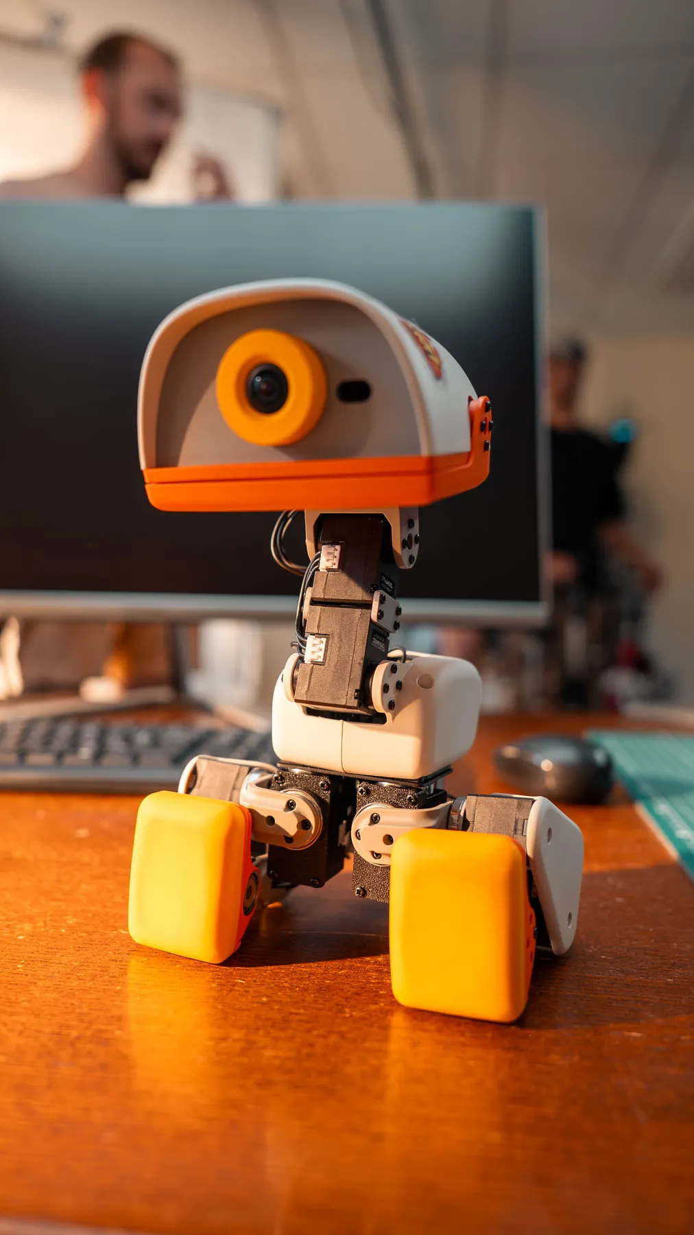 A seated MicroDuck robot on a desk in front of a computer.